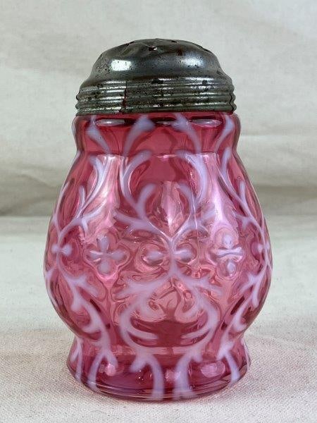 Fenton Sugar Shaker: Pink glass shaker in the Spanish Lace pattern, fitted with a metal lid and displaying a gentle aged patina. Measures approximately 4 3/4" H x 3" W x 3" D. In good condition with light surface wear con