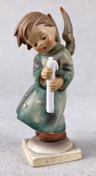 Goebel Hummel Heavenly Angel Figurine: Porcelain figurine depicting an angelic figure holding a Christmas candle, marked with the German Goebel Hummel stamp on the base. Measures approximately 6" H x 1 7/8" W x 1 7/8" D. Shows a repair to