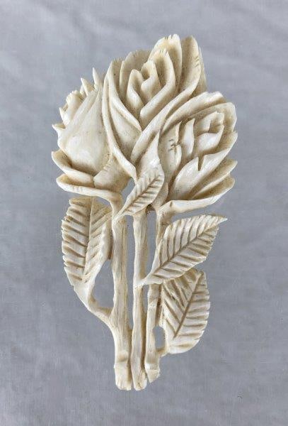 Carved Rose Bone Brooch: Carved bone brooch featuring an intricately detailed arrangement of stemmed roses with finely rendered leaves, displaying an attractive aged patina. Measures approx. 3" H x 1 5/8" W. In good condition