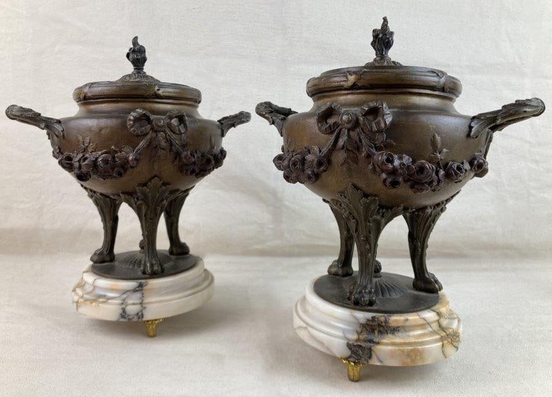 Pair of French Urns: A pair of French bronze urns set on marble bases with warm coloration, each raised on paw feet and decorated with intricate high-relief floral and foliate motifs. The urns display a rich, aged patina