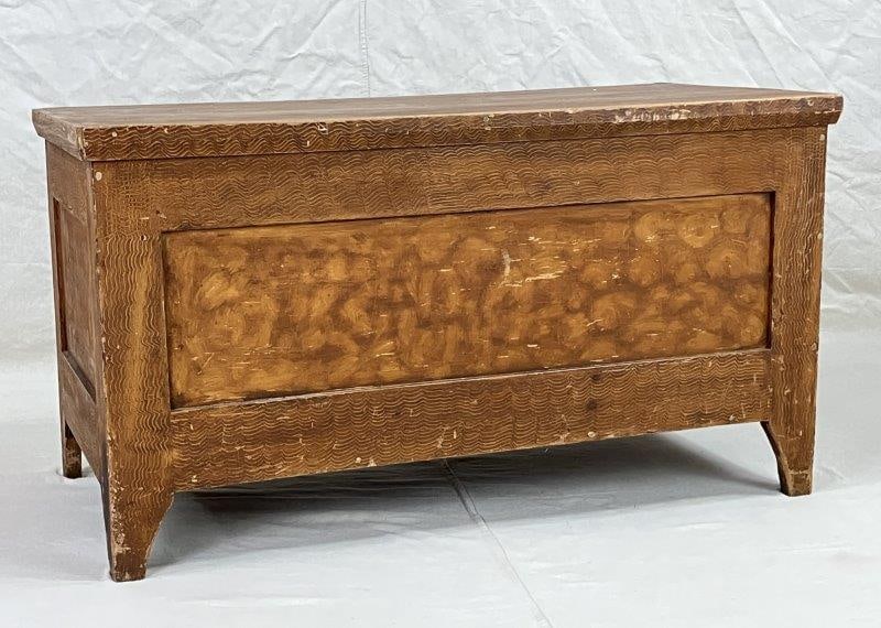 Grain-Painted Blanket Chest, Mid-19th Century: A mid-19th-century grain-painted blanket chest featuring tapered legs, a molded top, and remnants of old wallpaper lining the interior. The exterior retains a pleasing painted surface with period char