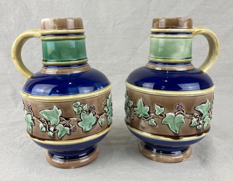 Pair of Wedgwood Majolica Jugs: A pair of Wedgwood majolica jugs dating to 1868, executed in a flagon-style form and impressed with the Wedgwood mark. Each jug is decorated with a grape-and-vine motif encircling the body, rendered i