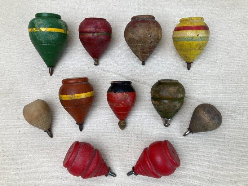 Vintage Spinning Tops: A group of vintage wooden spinning tops, some hand-painted with striped decoration and fitted with metal tips. The pieces display a worn, aged patina consistent with play and age. Various sizes. In go