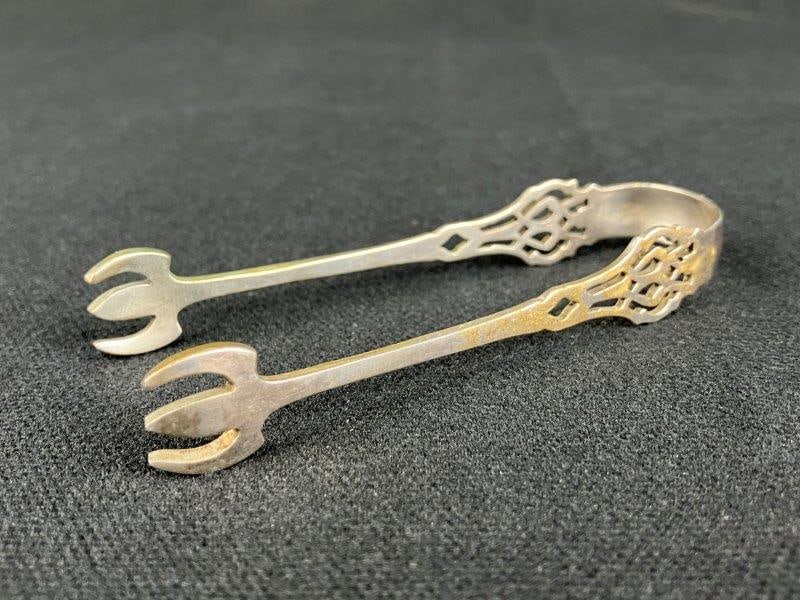 Sterling Silver Sugar Tongs: A pair of sterling silver sugar tongs featuring a claw-form terminal and Chippendale-style pierced decoration. The tongs display elegant period-inspired detailing with balanced proportions. Measures a