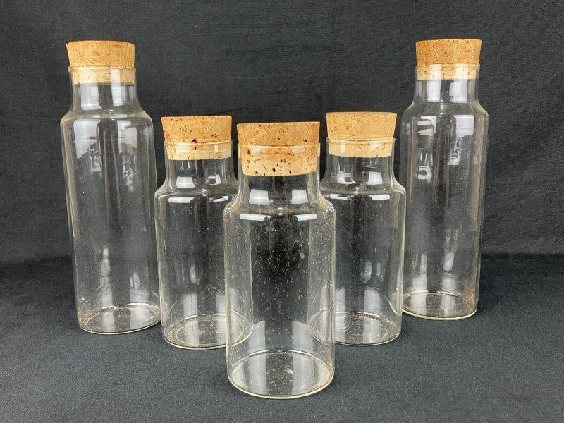 Apothecary Corked Glass Jars: A group of handblown glass apothecary storage jars fitted with cork lids, displaying simple utilitarian forms and natural irregularities from the glassmaking process. The tallest jar measures approxim