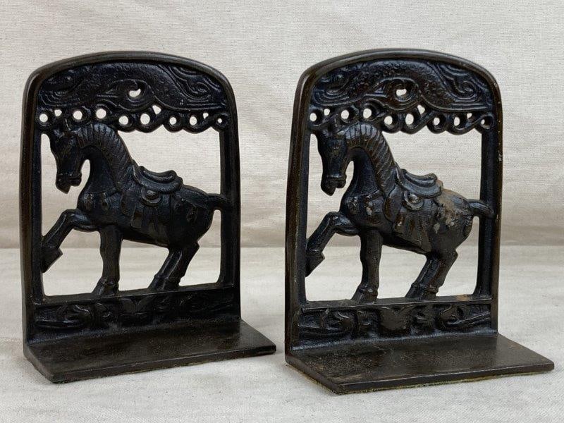 Cast Iron Equestrian Bookends: A pair of cast iron equestrian bookends featuring detailed saddled horse designs with a bird motif above each horse. The surfaces display a worn, aged patina. One bookend measures approximately 6̸
