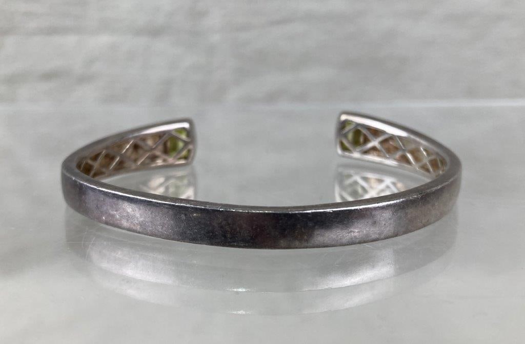 Sterling Silver and Peridot Cuff Bracelet: Sterling silver cuff bracelet featuring two baguette-cut peridot stones set at each open end, complemented by a subtle crisscross pattern along the interior of the band. Marked 925 to denote sterling
