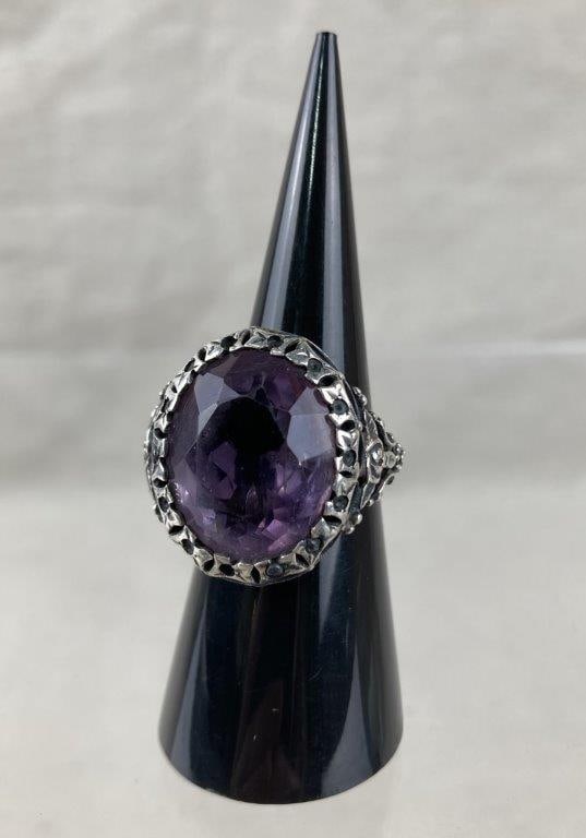 Art Nouveau Style Amethyst Ring: Sterling silver ring in an Art Nouveau style, set with a faceted oval-cut amethyst and framed by an intricate filigree setting with floral motifs. Displays a softly worn patina. Ring size approx. 8