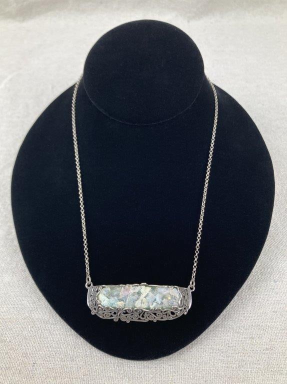 Paz Creations Roman Glass Necklace: Sterling silver necklace featuring iridescent Roman glass set within an ornate filigree design, showcasing vivid color play and textured craftsmanship. Finished with a magnetic barrel clasp and