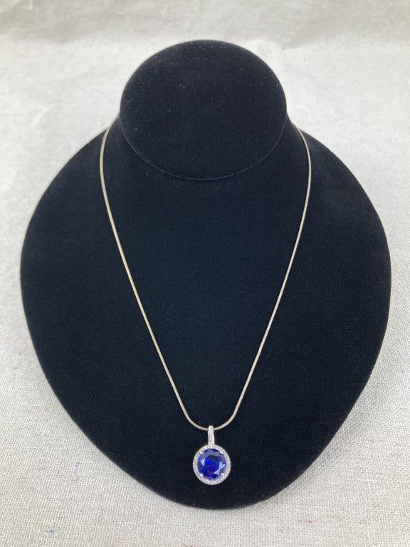 Sterling Silver and Tanzanite Halo Necklace: Sterling silver necklace featuring a central brilliant-cut faceted tanzanite stone surrounded by a halo of clear faceted accents, set within a raised filigree mounting; the decorative bail is also