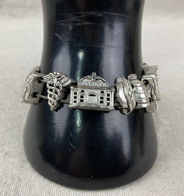 Silvertone Medical Nurse Slide Charm Bracelet: Silvertone slide charm bracelet decorated with medical-themed charms, including a hospital, rubbing alcohol bottle, bandages, gauze, and related motifs, making it an ideal novelty piece for someone in