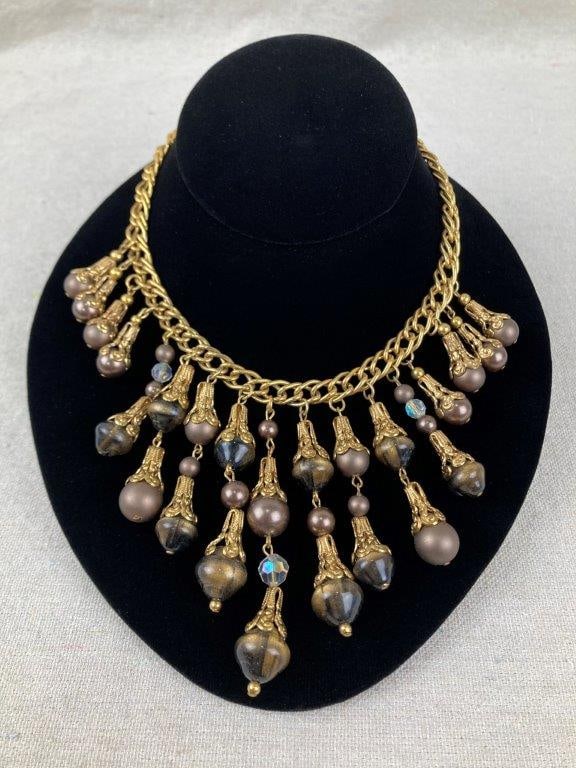 Goldtone and Faux Chocolate Pearl Costume Necklace: Goldtone costume statement necklace featuring an assortment of chocolate-toned faux pearls and warm brown glass beads, joined by a robust interlocking goldtone chain. Necklace measures approx. 12" L.