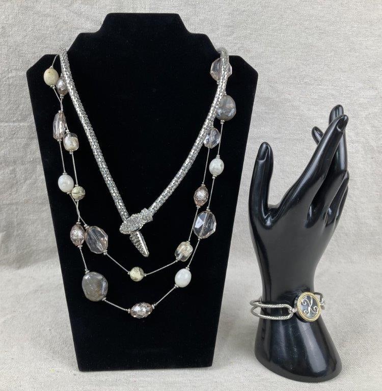 Three-Piece Silvertone Jewelry Assortment: Three-piece assortment of silvertone jewelry, including a bracelet featuring a central swirling script motif with a bead suspended beneath glass, a multistrand beaded necklace, and a snake-style neckl