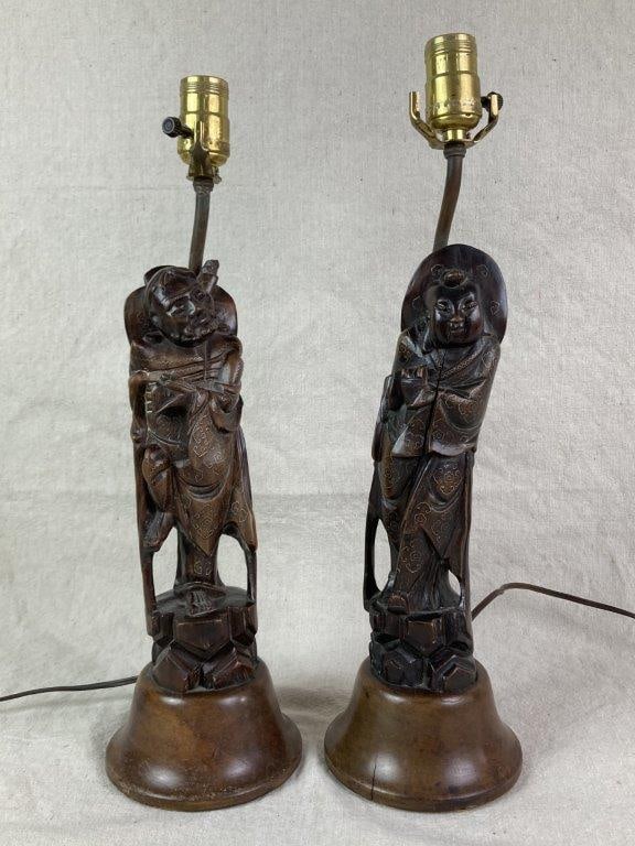 Chinese Carved Immortal Figure Table Lamps: Two hand-carved Chinese immortal figures converted into table lamps, each accented with inlaid silver and mounted on round wooden bases. Exhibits a worn, aged patina. The tallest measures