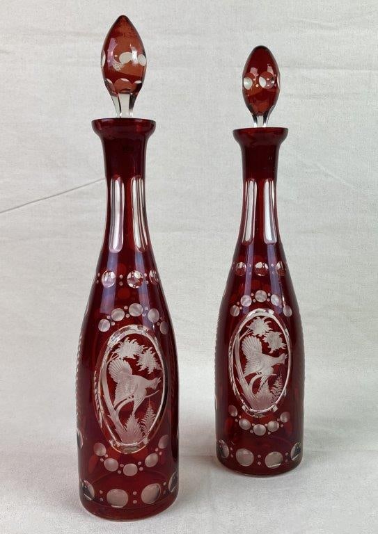 Bohemian Ruby Red Cut-to-Clear Crystal Decanters: A pair of Bohemian-style crystal decanters with ruby red overlay cut back to clear glass, each decorated with an etched bird motif. Fitted with matching glass stoppers. One decanter measure