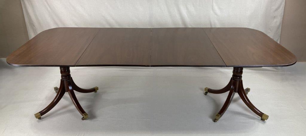 Fine Georgian Style Mahogany Table: A mahogany table in the Georgian style, featuring an expanding leaf form and a central turned pedestal base. The table is supported by characteristic legs with brass-capped feet. Measures