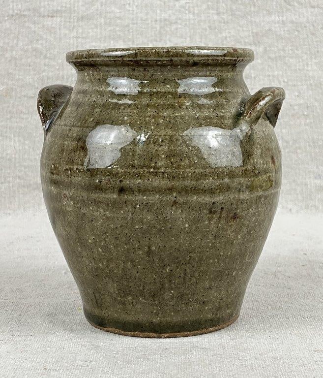 Edgefield Stoneware Jar By Genevieve Calmes: A Southern stoneware jar finished in a green alkaline glaze, featuring two applied handles. Bears the maker’s stamp with the initials “GC” to the side. Measures approximately 4 1/2"