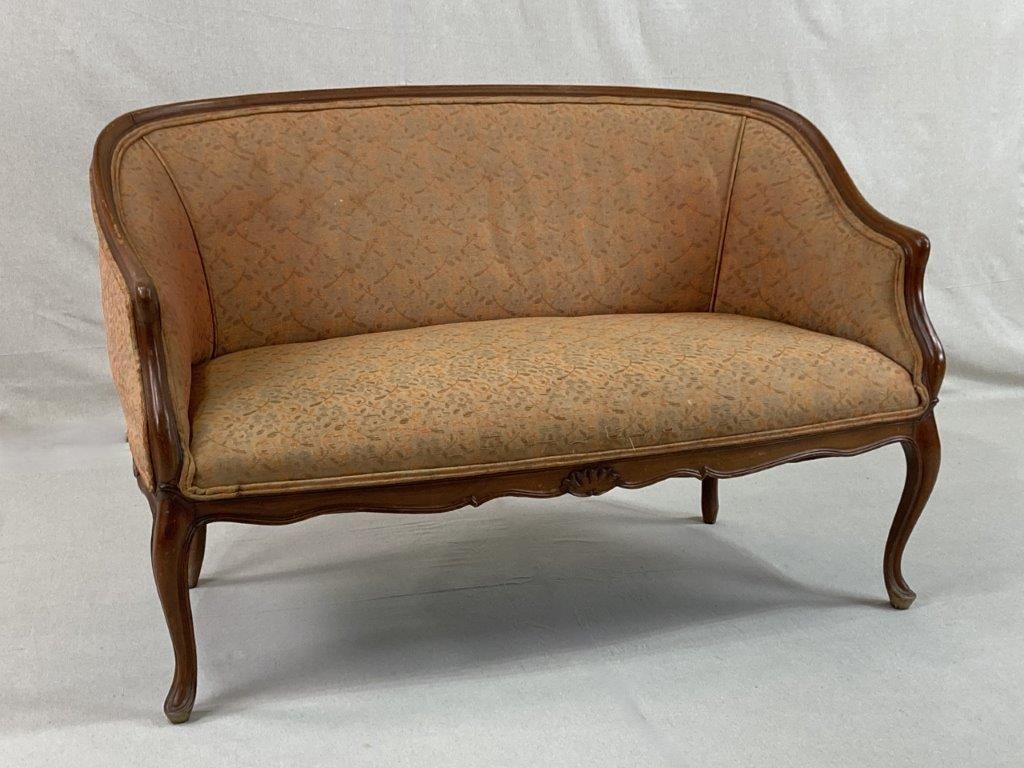 French Louis XVI Style Settee: A French Louis XVI style settee or loveseat featuring rich upholstery framed by warmly toned wood, centered with a carved shell motif and raised on delicately curving cabriole feet. The elegant lines