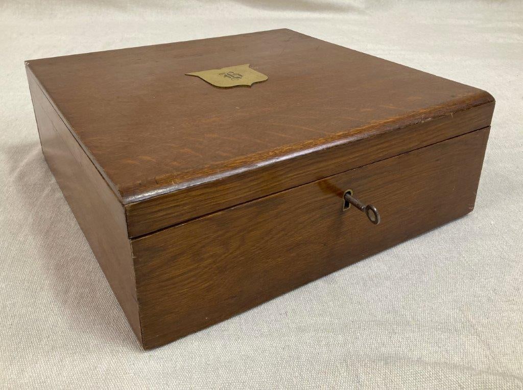 Mahogany Wood Writing Box: An antique mahogany writing box with rich, warm tones and a brass crest engraved with a monogram to the top. Retains its original key. Measures approximately 4 1/2″ H x 12 3/8″ W x 12 1/4&