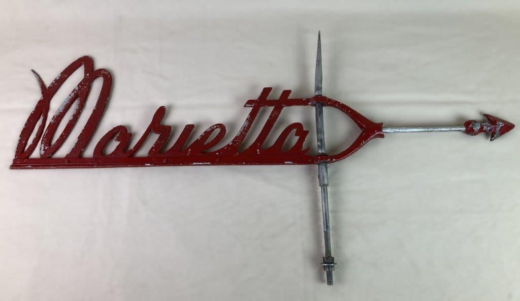 Marietta Weathervane: A red-painted cast aluminum weathervane featuring the name “Marietta” in flowing cursive lettering, originally designed as advertising for Marietta farm silos. Exhibits a worn, aged