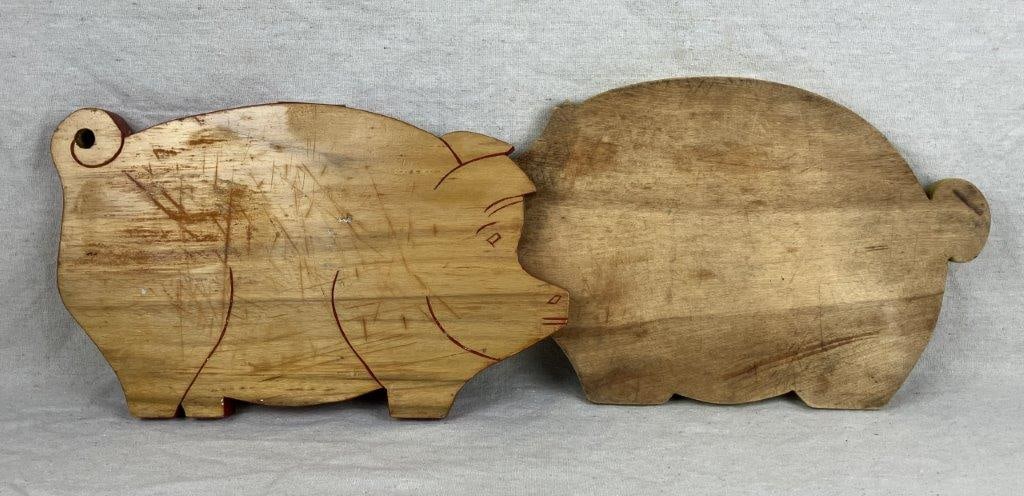 Two Vintage Wood Pig Cutting Boards: A pair of vintage pig-from wooden cutting boards, one with a red painted rim and incised details, the other with a yellow painted rim. Displays wear consistent with use and handling. The larger board