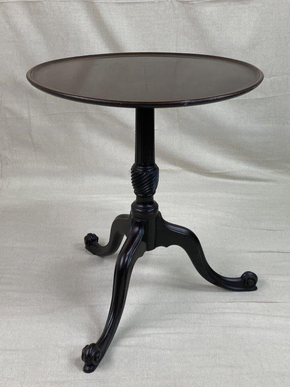 George III Mahogany Tripod Table: A George III mahogany tripod table featuring a round top with decorative inlay along the rim. Supported by a tripod base with three elegantly curved legs accented with spiral detail, further