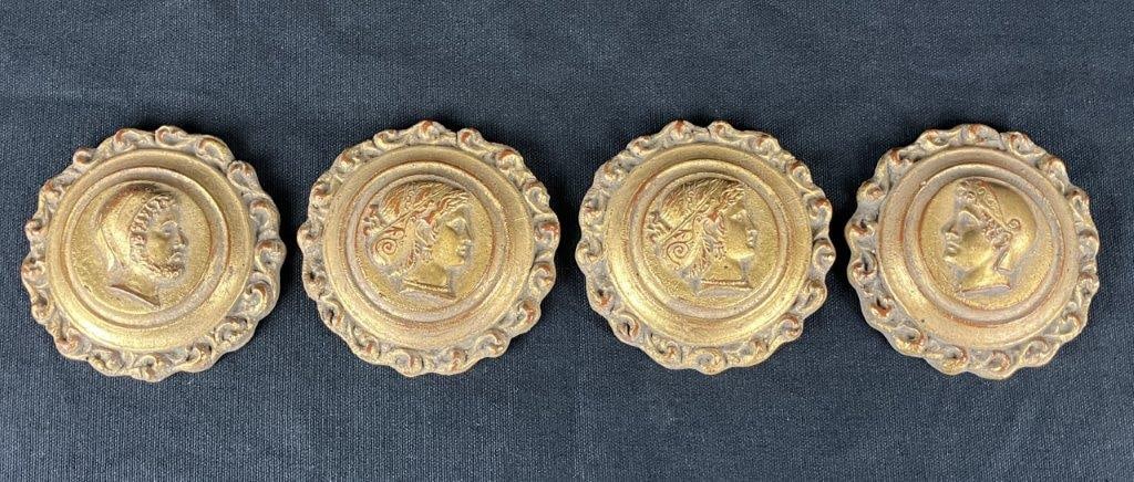 Four Gilt Classical-Style Medallion Wall Plaques: A set of four classical-style wall medallions, each featuring a relief bust of a Greco-Roman figure with gilt decoration. Each plaque measures approximately 1″ H x 4″ in diameter. In good