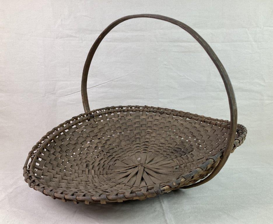 Country Flower Gathering Basket: A large country flower gathering basket with an oval-shaped body, wrapped rim, and arched handle. Exhibits a worn patina from age and use. Measures approximately 17″ H x 20 3/4″ W x 22