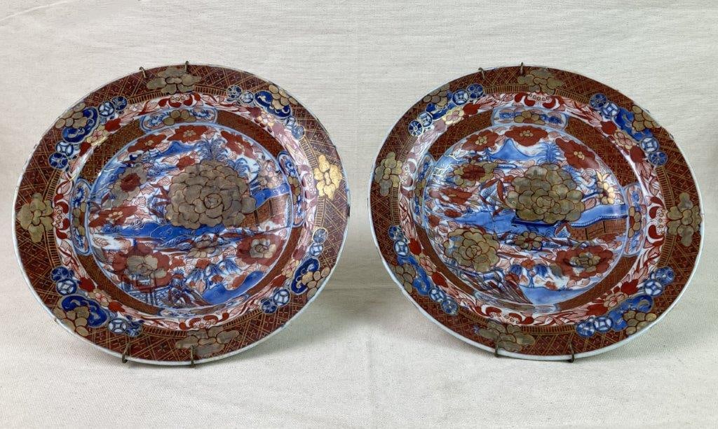 Two Japanese Imari Porcelain Plates: A pair of Japanese Imari porcelain plates featuring underglaze blue decoration with red and gold overglaze accents. Fitted with wall hangers on the reverse. Exhibits an aged patina. Each measures appr
