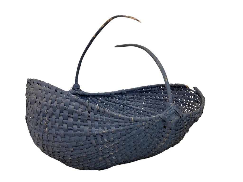 Blue Country Gathering Basket: A blue-painted split oak gathering basket with a boat-shaped body and wrapped rim, featuring woven diamond motifs at the base of the handles. Exhibits a worn, aged patina. Measures approximately