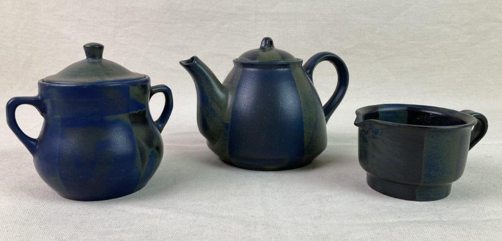 Nancy Patterson Lamb Blue Ridge Pottery Tea Service: A stoneware tea service by Nancy Patterson Lamb, comprising a lidded teapot, teacup, and lidded sugar jar. Features shaped handles and a distinctive hand-applied abstract glaze in layered blue and