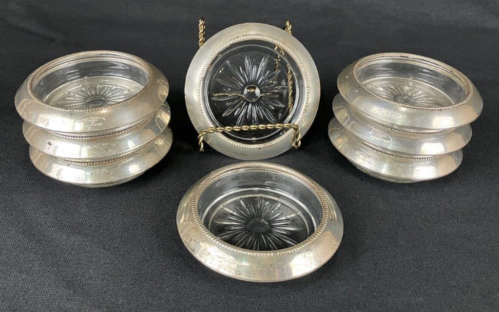 Frank M. Whiting & Co. Sterling Silver Coasters: A set of eight sterling silver coasters by Frank M. Whiting & Co., each fitted with a glass insert featuring a starburst pattern within the silver form. One coaster measures approximately