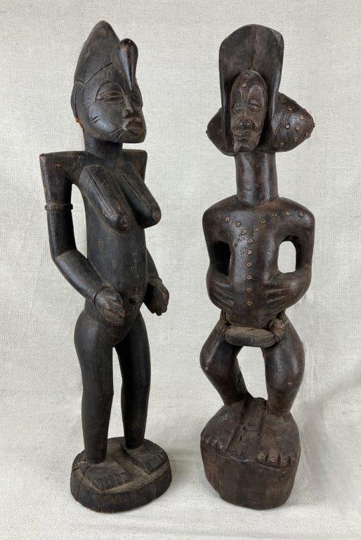 African Carved Wood Fertility Figures: A pair of carved wooden fertility figures from the Senufo people, depicting male and female forms symbolizing fertility and continuity. Each figure features an elaborate headdress and displays