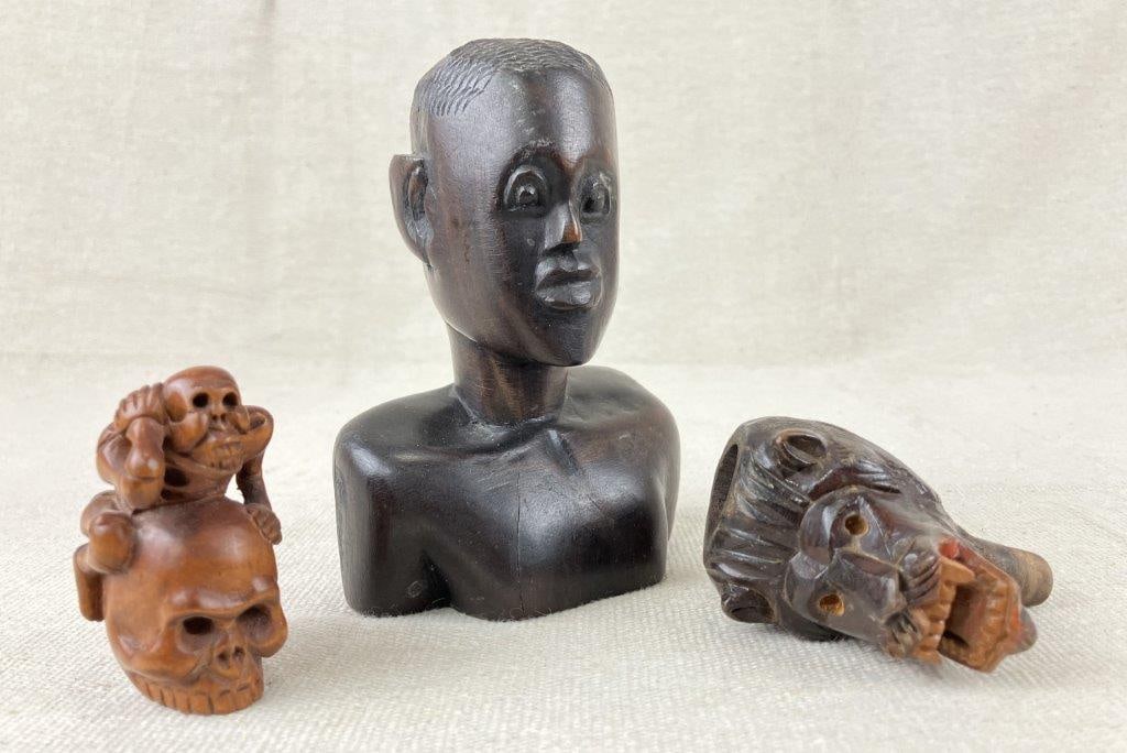 Folk Art Carved Figurines: A small group of folk art carved figurines, including a lionâ€™s head formerly used as a pipe component, a carved skull with skeleton motif, and a bust-form carving depicting an
