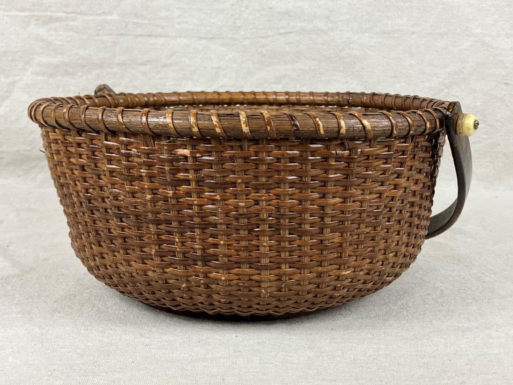 Nantucket Style Lightship Basket: A nicely woven rattan lightship-style basket with an attached handle fitted with white knobs, a wrapped rim, and a round wooden base. Displays a warm, even patina. Measures approximately 4