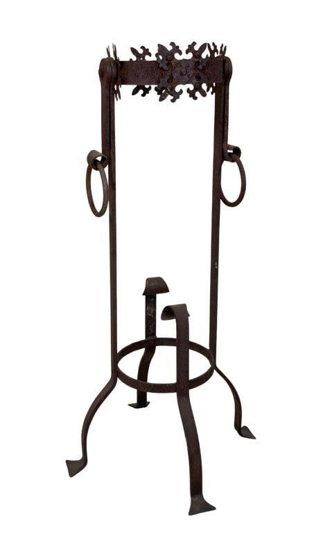 Antique Wrought Iron Fireplace Tool Stand: An antique wrought iron fireplace tool stand featuring ornate decorative accents along the top rim, two ring handles, and four supporting legs. Exhibits a worn, aged patina. Measures approximately 34&