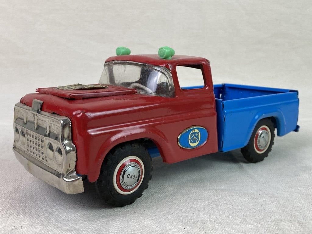Vintage Marusan "Bulldog" Toy Truck: A red and blue tin and pressed-steel pickup truck made by Marusan, featuring lithographed details. Marked â€œFordâ€ on the wheels and tailgate, with a hood sticker rea