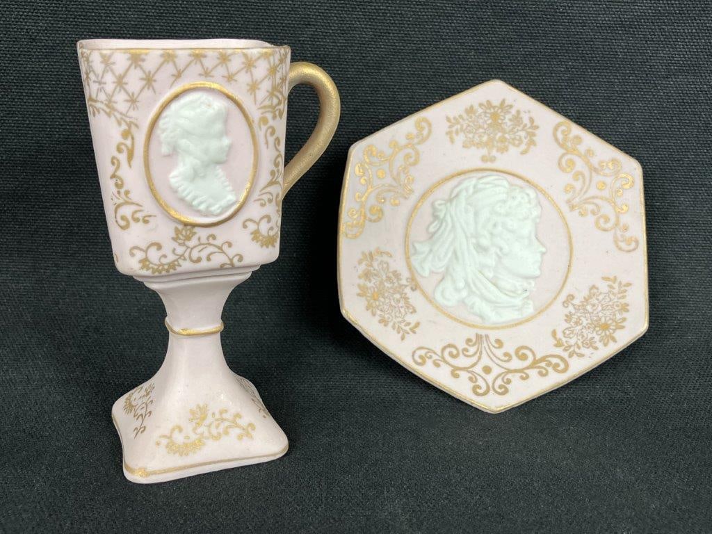 Light Pink Bisque Cameo Cup and Dish: A delicate bisque porcelain cup and dish set featuring an applied cameo medallion accented with surrounding gilt detailing, set against a soft pink ground. The cup measures approximately 4 1/4″