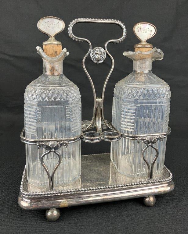 Cruet Set: A complete cruet set comprising two decanters, one intended for port and the other for brandy, with space for mixing utensils and housed in a silver plate caddy. Measures approximately 11″ H x