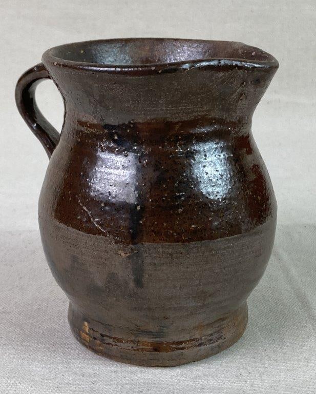 Small Stoneware Pitcher: A brown-glazed stoneware pitcher featuring a squat, rounded body with a flared rim and an applied handle. Exhibits an aged patina. Measures approximately 4 1/2â€³ H x 3 1/2â€