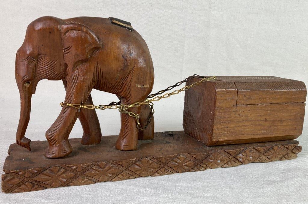 Carved Elephant with Trinket Box: A hand-carved elephant figurine mounted on an ornate carved base, accompanied by a hinged trinket box connected to the figure by a gold-tone chain. The box features incised linear decoration and a