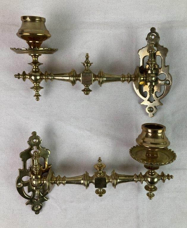 Brass Piano Candle Holders: A pair of solid brass piano candle holders featuring ornate decorative backplates, a central stem with decorative turnings, and a swinging arm designed for piano mounting. Retains a warm, aged