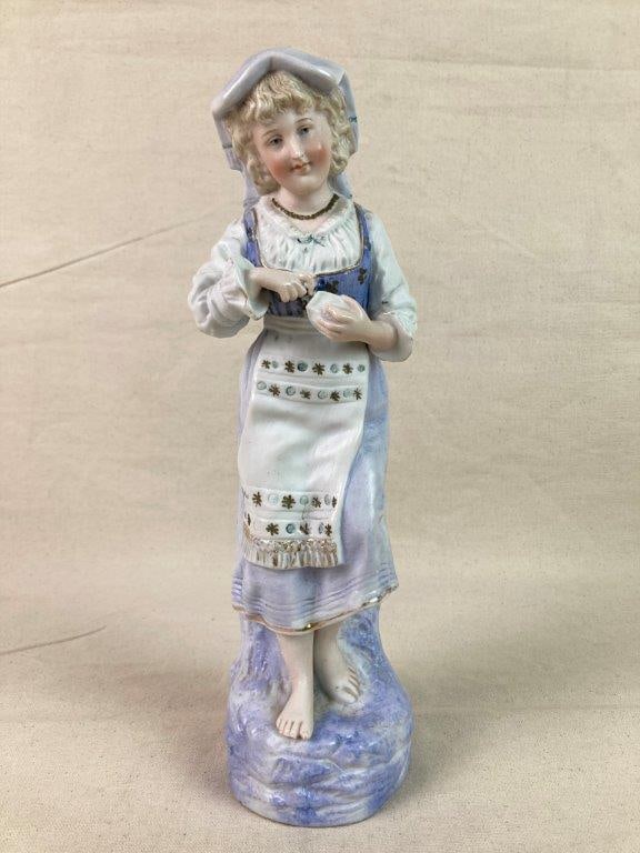 German Bisque Porcelain Figure of Young Girl: An German bisque porcelain figure depicting a young girl, finished with hand-painted details in a soft matte surface and accented with gold-tone highlights. Set upon a modeled tree log base. Measures