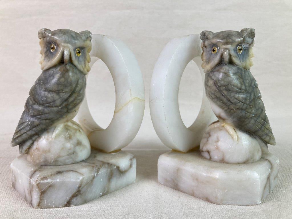 Carved Alabaster Owl Bookends: A pair of carved alabaster bookends depicting owls perched atop half-sphere bases, accented with round white ring details and designed to resemble marble. Each features applied glass eyes and