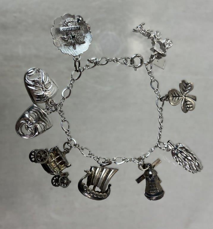 Vintage Sterling Silver Charm Bracelet: Sterling silver charm bracelet featuring a collection of figural charms including comedy and tragedy masks, a clover stamped DGC for Daniel George Collins, a pinecone stamped Sterling, and a Viking