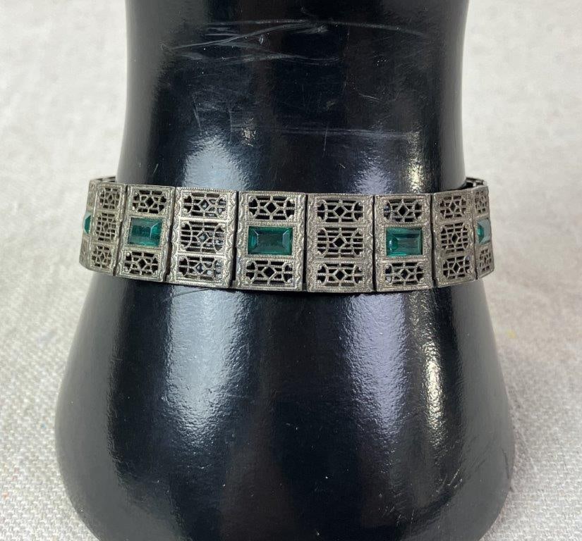 Simmons Sterling Silver Art Deco Bracelet: Simmons sterling silver bracelet dating to the 1920s, designed in the Art Deco taste with baguette-cut emerald-toned stones set within pierced filigree openwork panels. Fitted with a box clasp.
