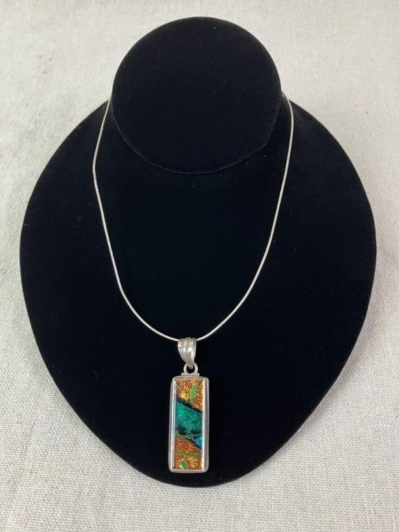 Artisan Sterling Silver and Art Glass Pendant Necklace: Artisan necklace featuring a vibrant art glass pendant displaying iridescent greens, blues, and golden tones, housed within a sterling silver setting and suspended from a simple sterling chain. Chain