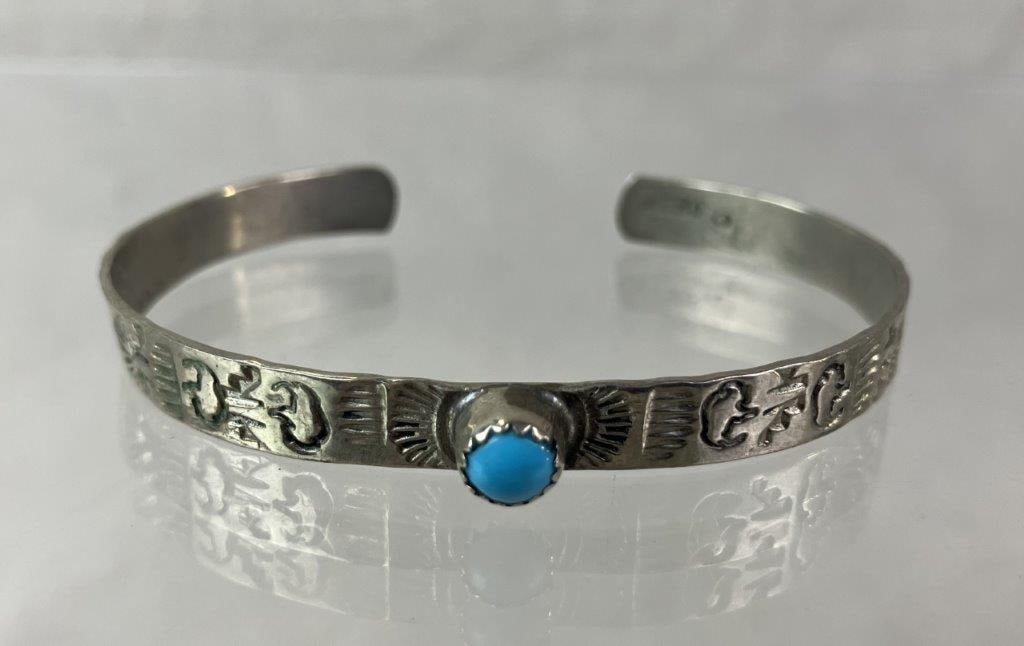 Native American Sterling Silver and Turquoise Cuff Bracelet: Native American cuff bracelet featuring hand-stamped sterling silver designs along the band centering a turquoise cabochon. Interior bears a feather emblem artist mark with a “C”; tested
