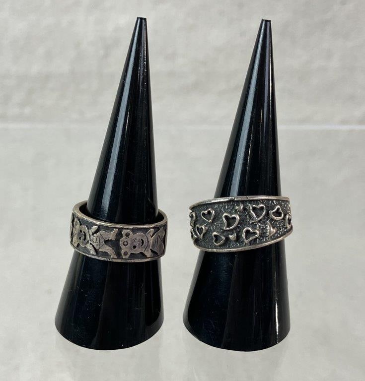Two Sterling Silver Rings: Two sterling silver rings featuring raised relief decoration, including one band adorned with repeating heart motifs (ring size approx. 9) and another with repeating figurative forms (ring size approx