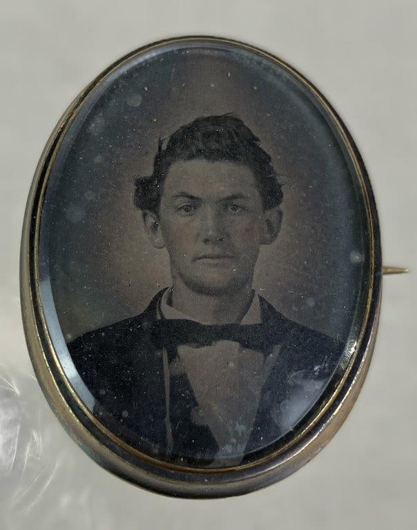 19th Century Mourning Brooch: 19th century oval mourning brooch featuring a portrait of a finely dressed gentleman beneath a glass cover, mounted in a gold-tone setting. Measures approx. 1 5/8" H x 1 1/4" W. In age-appropriate